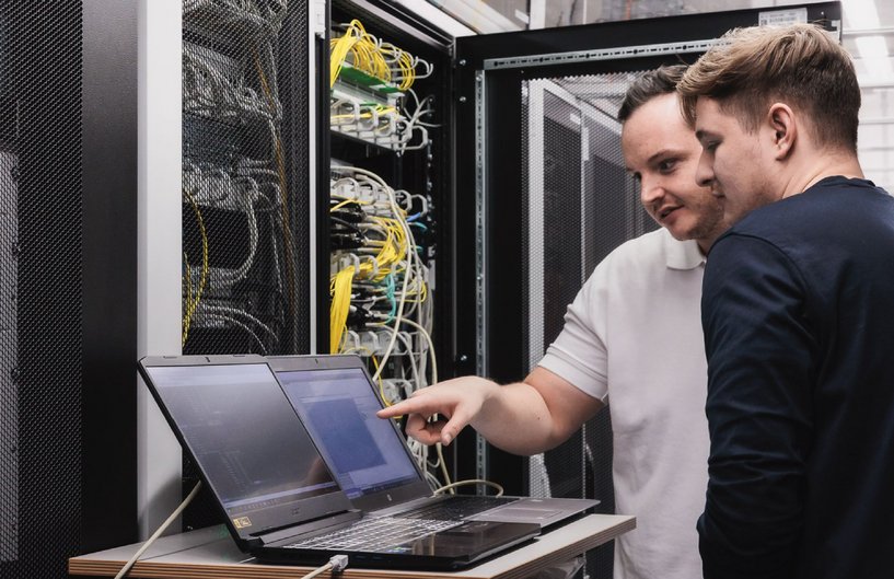2 Männer reden gemeinsam im Serverraum über Laptop 2 Männer reden gemeinsam im Serverraum über Laptop