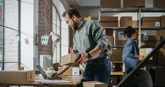 Unternehmer mit Packet in der Hand arbeitet am Laptop Unternehmer mit Packet in der Hand arbeitet am Laptop